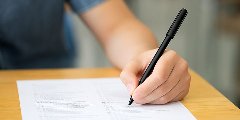 a person using their left hand to write on an exam paper